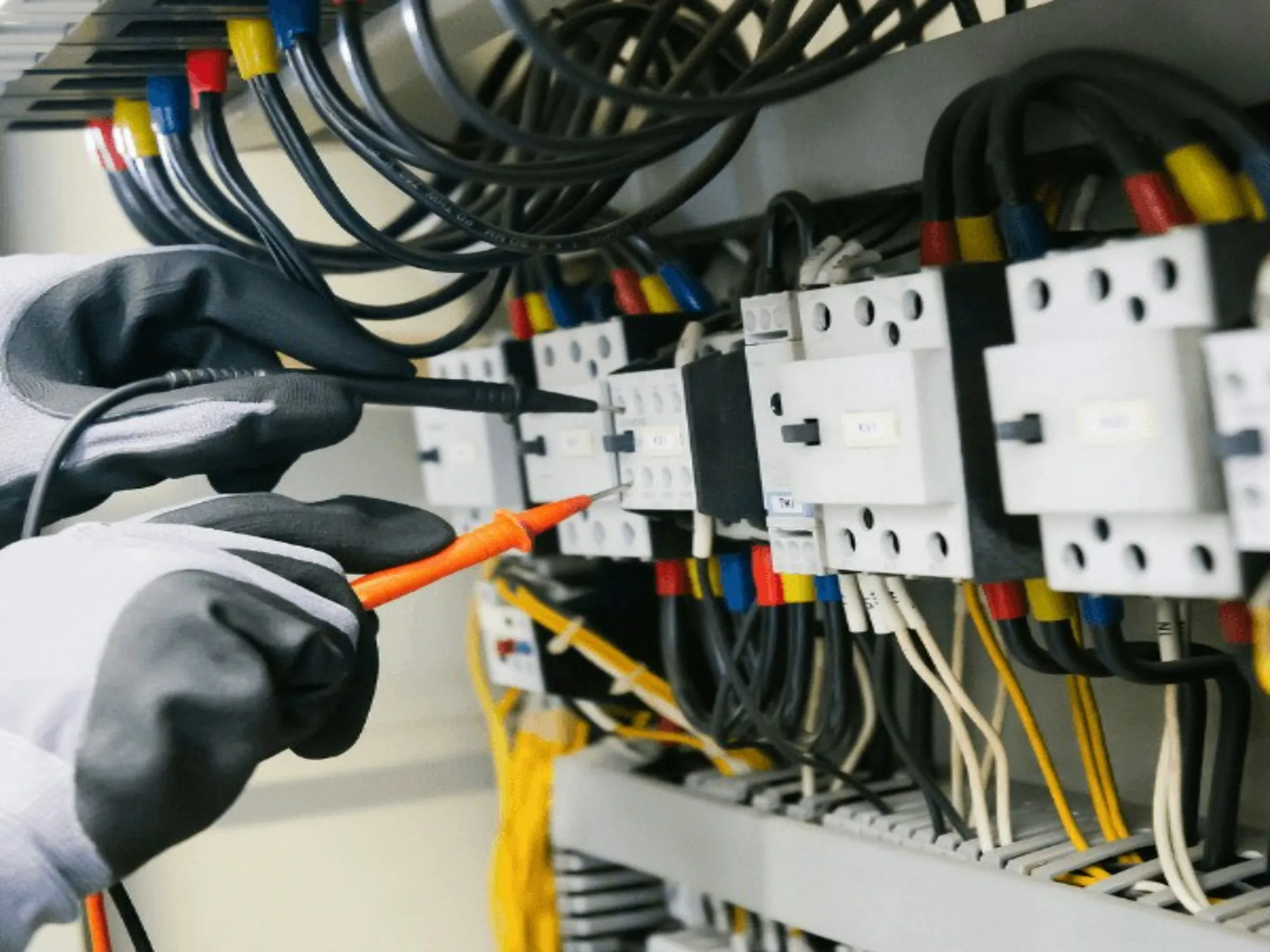 Gloved hands testing control wiring with a voltage tester